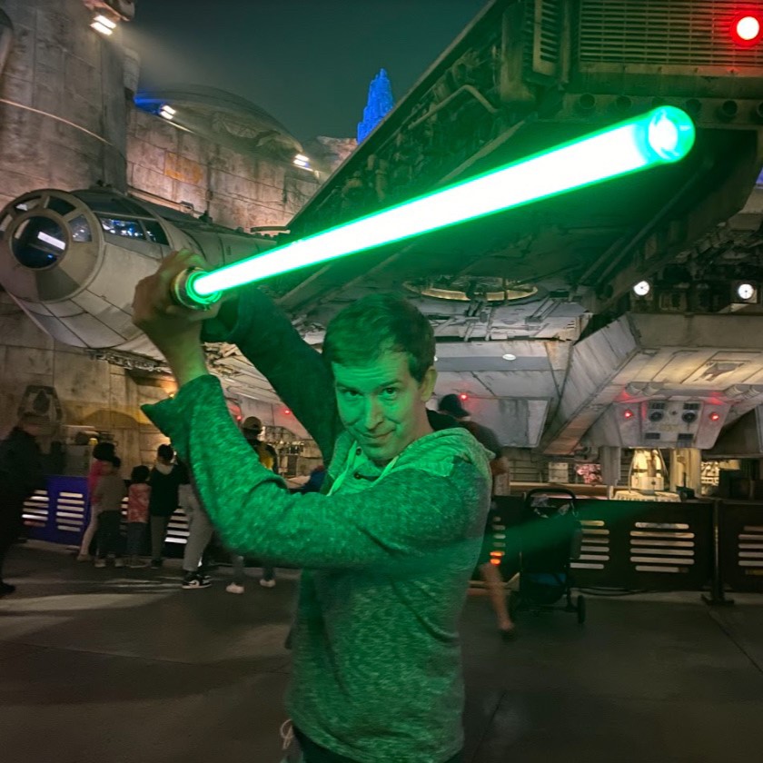 Charles weilding a lightsaber outside the Falcon at Galaxy's Edge.