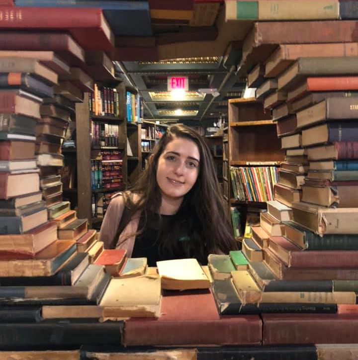 Kendra posing in a library with a circle of books stacked around her.